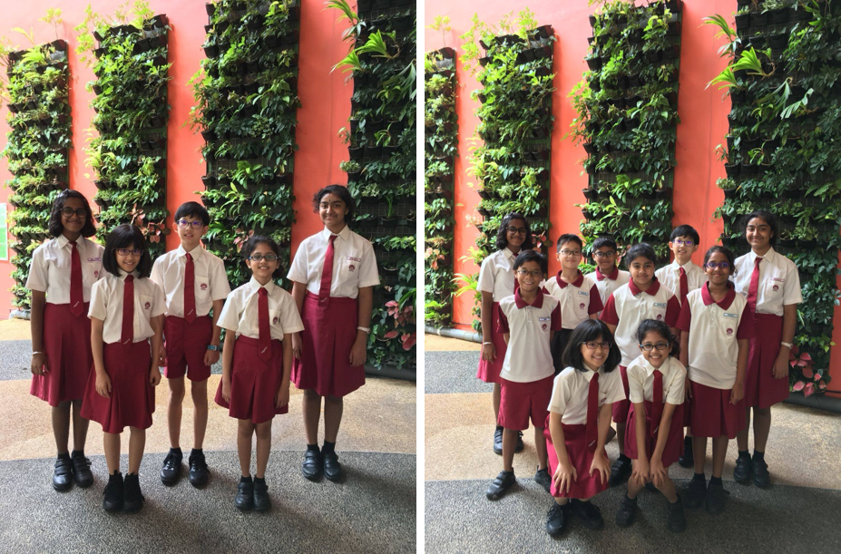 Students in white and red uniforms pose in front of a green plant wall on an orange building.